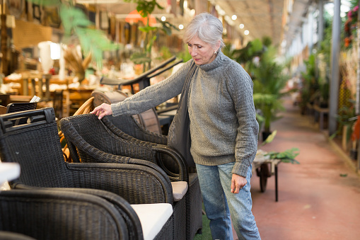 Senior woman looking for plastic rattan garden furniture in store