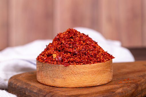 Chilli pepper seedless flakes in wooden bowl. Spices and food ingredients. Close up