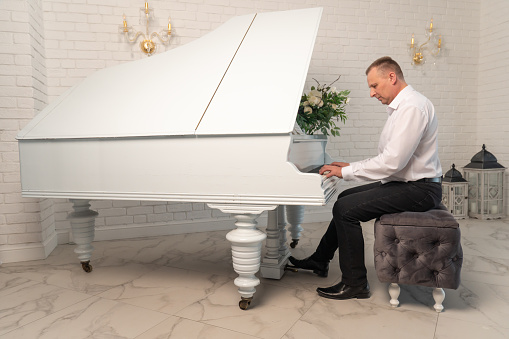 Мужчина играет на пианино в белом интерьере. Понятие классической музыки.