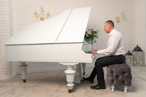 Мужчина играет на пианино в белом интерьере. Понятие классической музыки.