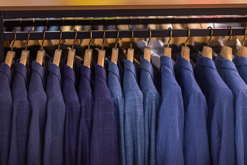 A number of men's suits on hangers in a company store