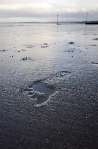 Bare footprint in the sand on beach on cloudy day in autumn. Portobello beach, Edinburgh, UK.