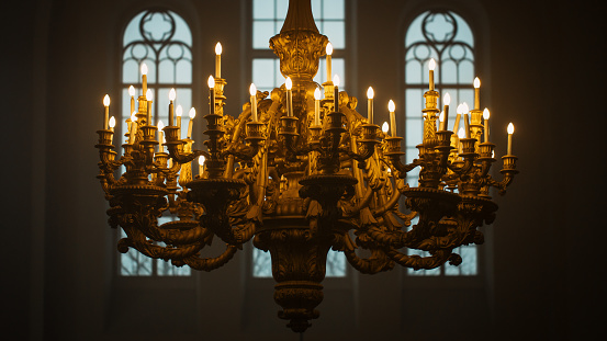 Close Up Shot of a Majestic Golden Chandelier Hanging from the ceiling of a Grand Church. An Antique Piece of Rococo Style Decorates the Cathedral and Lends Light to the Interior of the Building