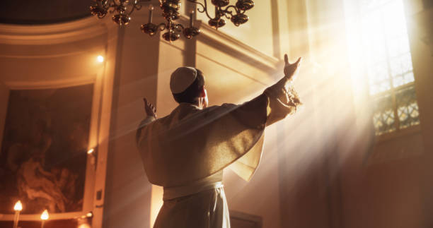 o papa levanta as mãos num gesto de bênção universal, enquanto é luminoso pela orientação de deus. ele está levantando as mãos para o céu como um sinal de devoção total ao senhor - we have a pope - fotografias e filmes do acervo