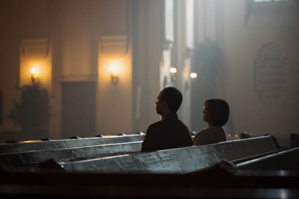 two people siting in church, praying and feeling a connection to god. man and woman believing in the goodness and kindness and finds solace in spirituality and religion, contemplating faith - confession religion imagens e fotografias de stock