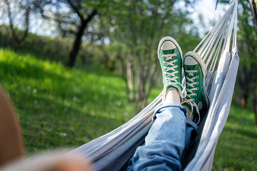 Women's legs shod in green sneakers on a hammock in a summer garden. Summer holidays vacation concept