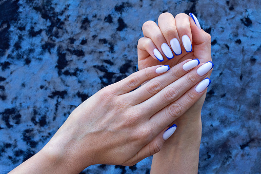 The hands of a young woman with beautiful nails after a nail salon with a French manicure in white and blue. Copy space.