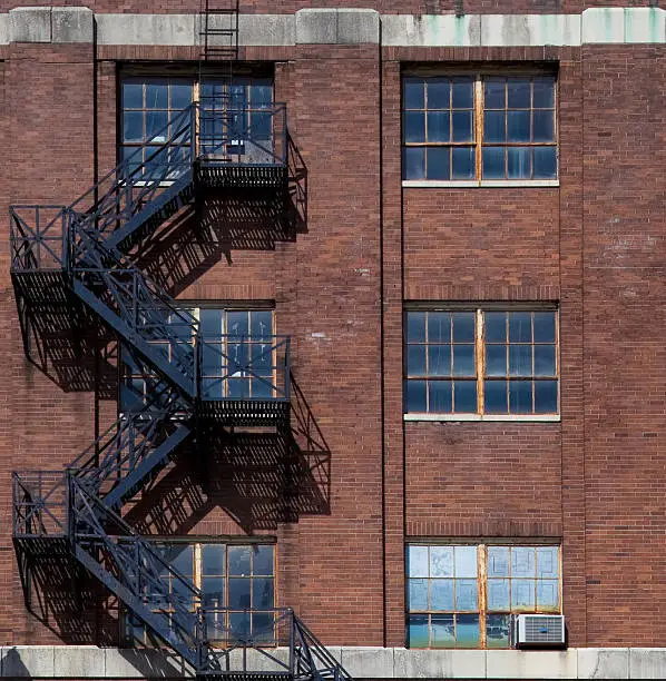 Metal fire-escape stairs on the outside of an old brick industrial building.