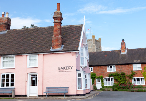 View of the centre of Orford village showing a Bakery advertising 'real bread and slow food', a row of terraced cottages and the church tower in the background.