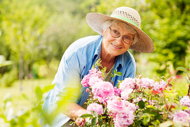 senior mujer con flores en el jardín - mujeres mayores fotografías e imágenes de stock
