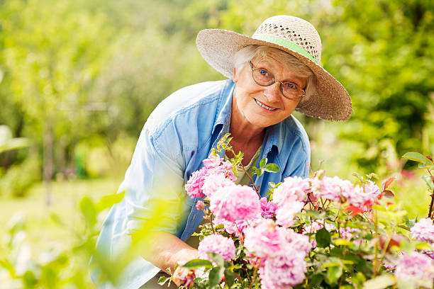 senior donna con fiori in giardino - mature women foto e immagini stock