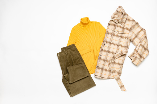Female winter or autumn stylish clothing set. Plaid checkered shirt, yellow sweater, green corduroy trousers. Trendy fashionable casual clothes. Fashion concept. Flat lay, top view.
