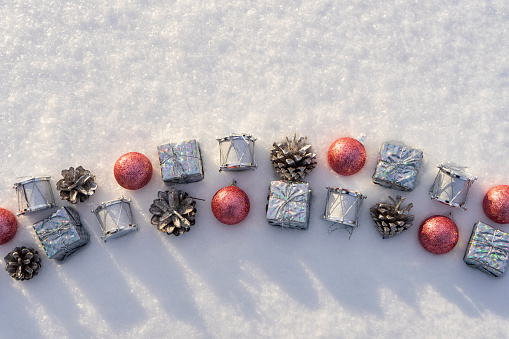 Merry Christmas and Happy New Year. New year toys lying on fresh white sparkling snow on sunny winter day. Silver gifts and drums, pine cones, pink balls. Merry Christmas concept. Top view, copy space