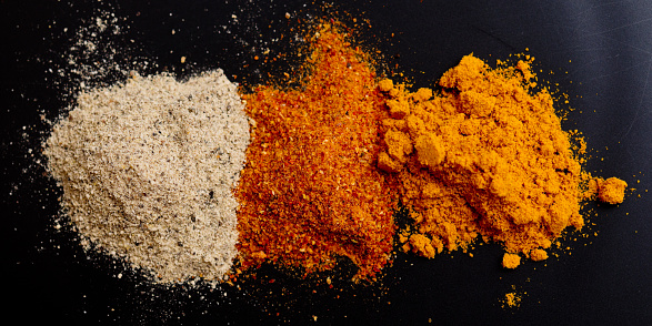 Turmeric, paprika, white pepper on black background, top view