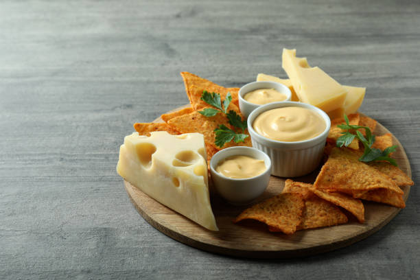istock Board with cheese sauce, chips, cheese and parsley on gray textured table 1482792036