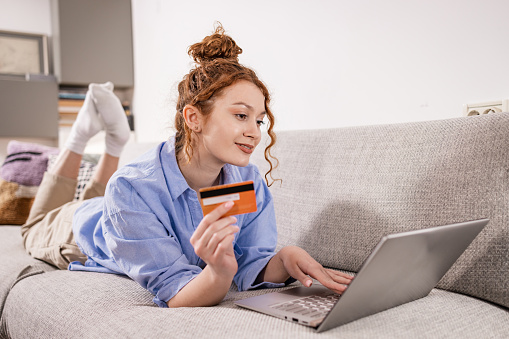 Young woman relaxing on the sofa and using laptop for online shopping.