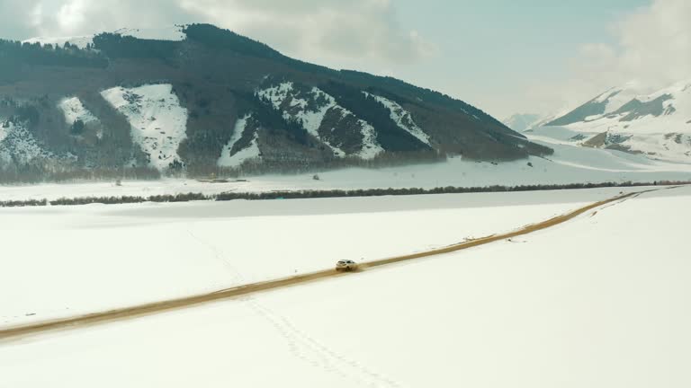 a white car driving on a dirt road next to a snow-covered roadside among the mountains