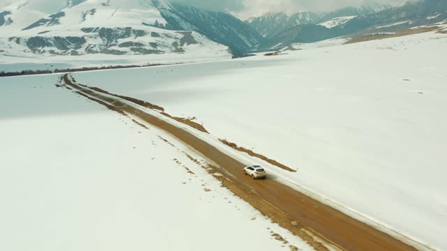 a white car driving on a dirt road next to a snow-covered roadside in the mountains