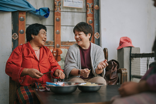 Asian Chinese female tourist experiential travel cutting potato in Bhutanese farmhouse preparing food for dinner with Bhutanese Senior woman