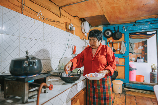 Bhutanese Senior Woman cooking in kitchen preparing traditional food for family dinner in farm house
