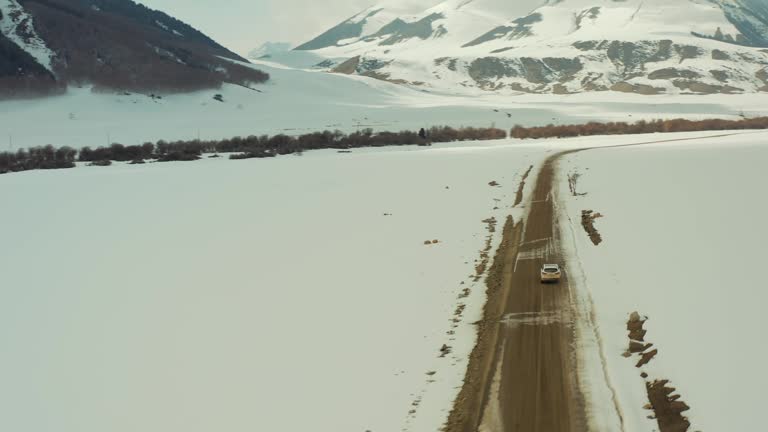 a white car passing on a dirt road with snow in the mountains