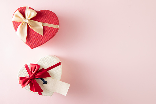 Heart shaped gift boxes with red ribbon and empty gift tag on pink background