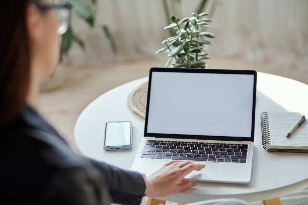 istock Mockup white screen laptop and mobile phone woman using computer sitting at table at home, back view 1482796870