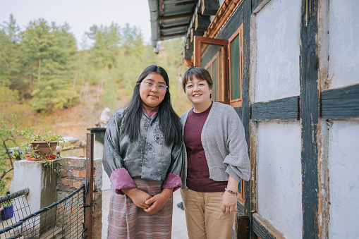 portrait Asian Chinese female tourist and Bhutanese teenage girl outside farmhouse