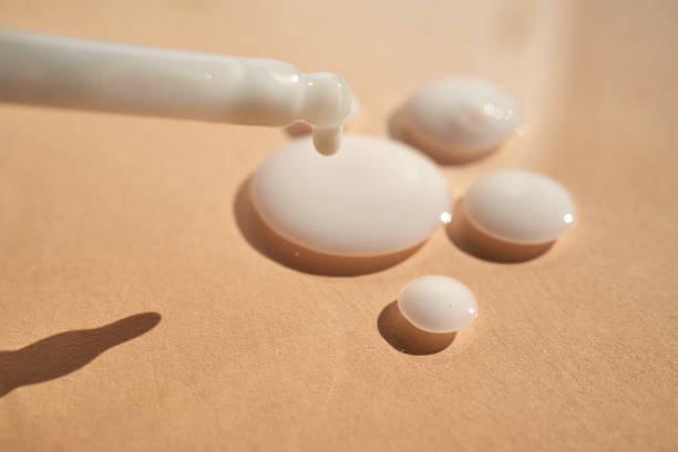 Drops of white cosmetics on a beige background with a dropper.