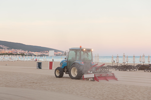 Evening empty beach. Tractor smoothes the sand on public beach by the sea