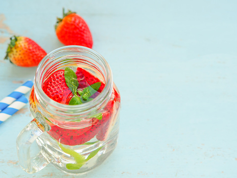 Infused water of strawberry in mason jar and straw on blue wooden table. Healthy drink, Top view, space for your text.