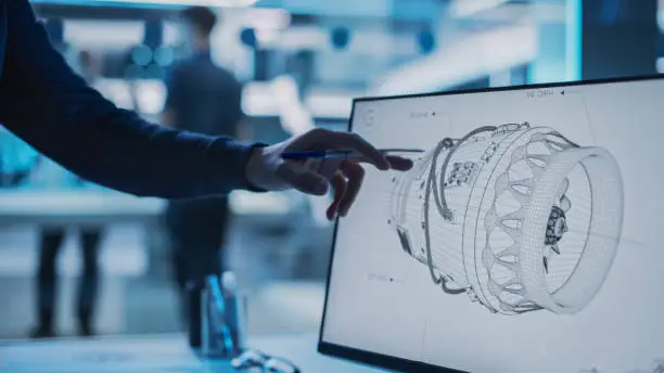 Close Up of a Desktop Computer Monitor Screen with 3D CAD Software with Prototype Jet Engine Project. Specialist Discussing Work, His Hand Visible In Front of the Screen.