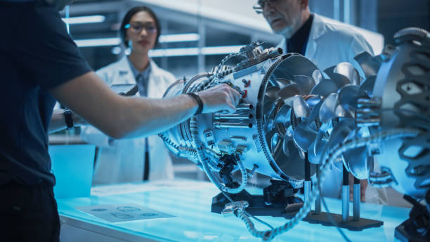 istock Diverse Multiethnic Team of Industrial Engineers Gathered Around a Table With a Prototype Turbofan Engine. Scientists Discuss the Futuristic Motor, Use Equipment and Tablet Computer for Research. 1482800063