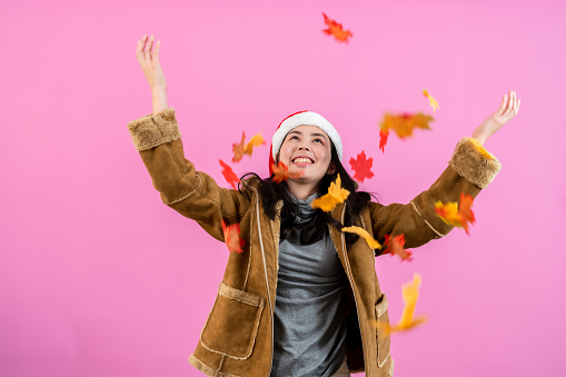 girl was wearing thick long-sleeved shirt that covered body from cold air, was an excited expression on leaves had fallen from tall trees around, Isolated indoor studio on pink background.