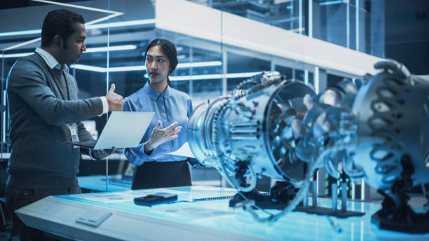 istock Two Multiethnic Employees Work in Modern Innovative Research Facility with a Futuristic Jet Engine. Engineer with a Laptop Explaining How the Prototype Motor Works to an Industrial Specialist. 1482801951