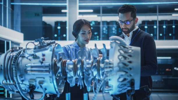 istock Two Multiethnic Employees Work in Modern Innovative Research Facility with a Futuristic Jet Engine. Engineer with a Laptop Explaining How the Prototype Motor Works to an Industrial Specialist. 1482801990