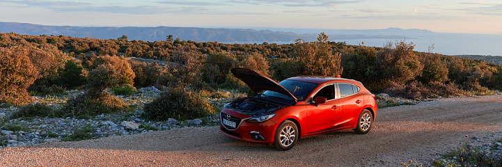 Red Mazda 3 with an open hood is standing during a holiday tour of a island. Sunset, no people. Brac Island, Croatia - 05.31.2019
