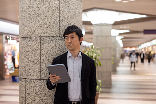 Japanese businessman holing laptop and waiting for someone in city
