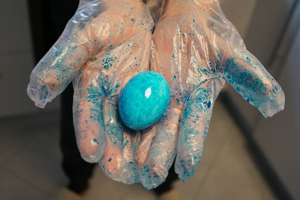 istock Painting eggs for Easter. A man in a glove holds an Easter egg. Blue Easter egg in hand. Different types of color of eggs for Easter. A blue-colored egg in the hand, in a glove. 1482804697