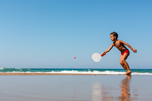 Boy playing beach tennis on a flat sandy beach