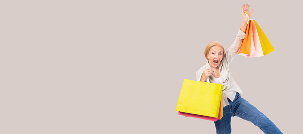 Cheerful excited older woman holding shopping bags Excited elderly lady with raised hands celebrating success Portrait cheerful positive senior female with raised hands and fists open mouth copy space