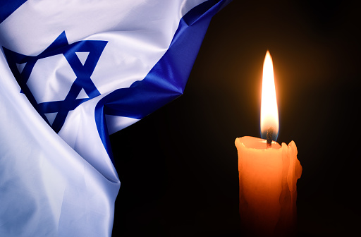 Holocaust Remembrance Day. Yom HaShoah. Bright Burning Candle and the official flag of Israel on a dark grey background. Memorial Day for Jewish people.