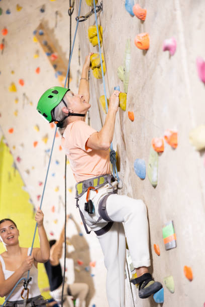 ジムで人工ロッククライミングの壁を登るポジティブな筋肉の引退した女性 - climbing mountain climbing rock climbing women ストックフォトと画像