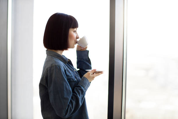 istock Woman with coffee cup enjoying view from panoramic window 1482814396