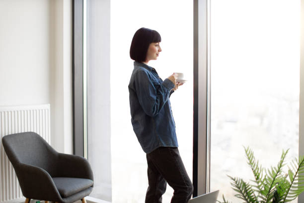 istock Woman drinking coffee and looking at window at office 1482814405