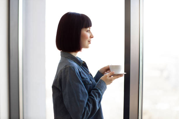 istock Woman drinking coffee and looking at window at office 1482814406