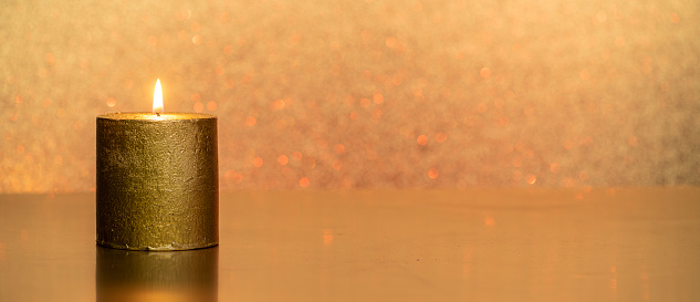 a golden candle in front of a golden glittering background  for banner, panorama or border with copy space