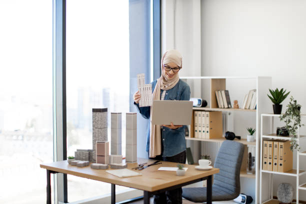 istock Employee holding computer and scale model in office inerior 1482827244