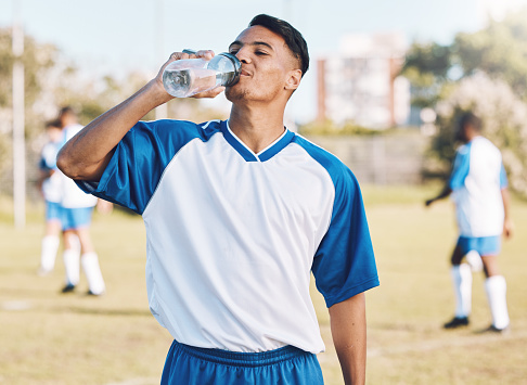 Drinking water, break and soccer player on a sports field resting after match or competition on a sunny day. Man, athlete and sportsman refreshing during a game happy and smiling for due to fitness