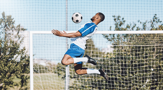 Sports, soccer and man in action with ball playing game, training and exercise on outdoor field. Motivation, workout and male football player for defence, goalkeeper and jumping for goals for fitness